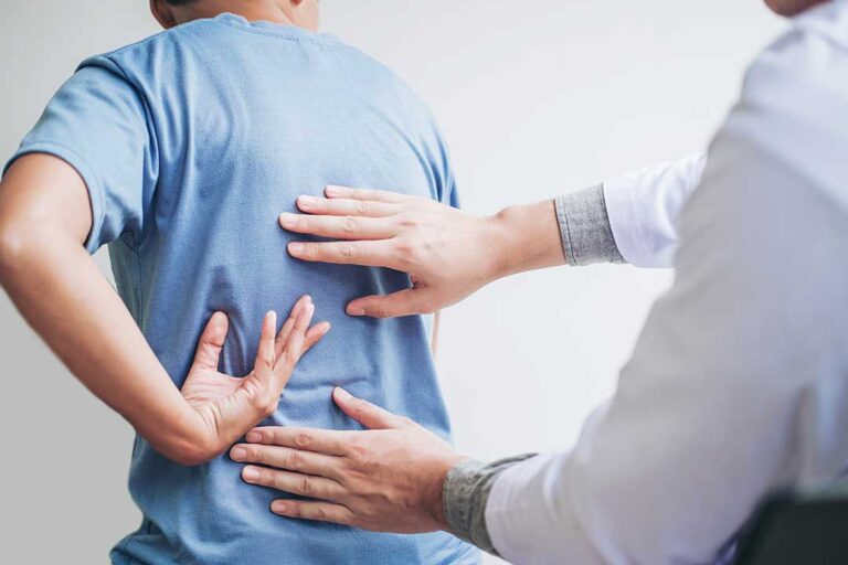A therapist works on a patient’s back while a spine model and treatment table sit nearby.
